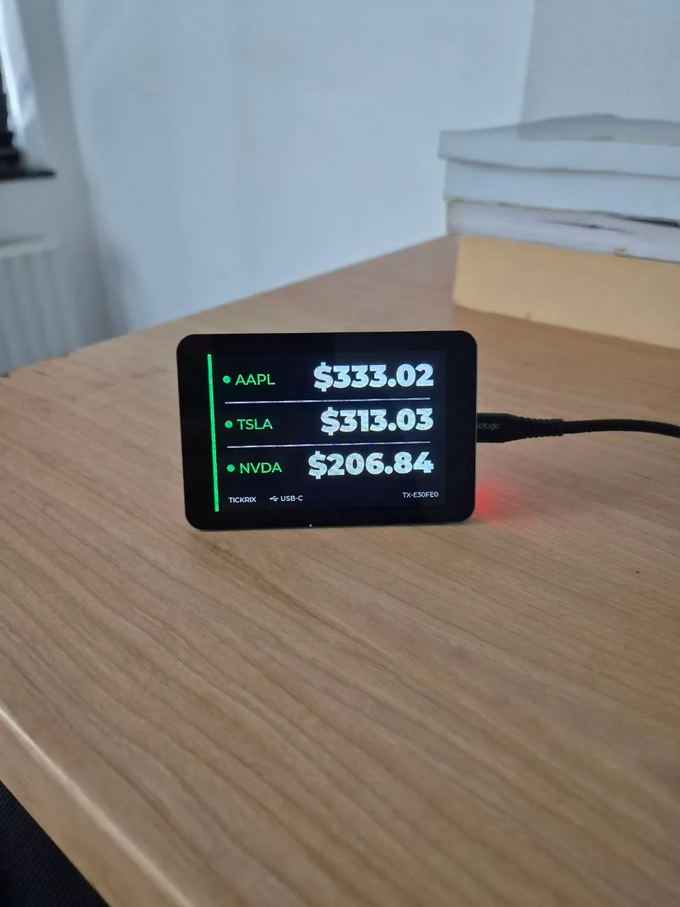 A Tickrix stock ticker display on a desk showing live AAPL, TSLA and NVDA prices